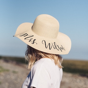 Puede incluir: Un sombrero de paja para el sol con un ala ancha y texto negro que dice "Mrs. Wilson".