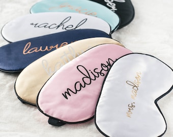 May include: A set of seven personalized sleep masks in various colors, including white, pink, beige, blue, and light blue. Each mask has a different name embroidered on it in black or gold lettering. The names include "rachel", "laure", "madison", "mrs. madison", "kathle", and two others that are not visible.