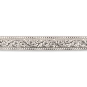 May include: A silver metal band with a decorative, engraved design. The band has a repeating pattern of swirls and dots.