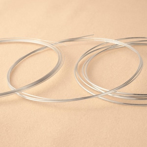 May include: Silver wire coils, arranged in two groups on a beige surface. The wire is thin and shiny.