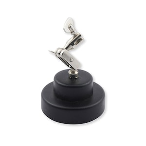 May include: A silver-colored metal alligator clip mounted on a multi-jointed, adjustable arm attached to a solid, circular black base. The articulated arm features a swivel mechanism at the top, allowing for precise positioning of the metal clip.