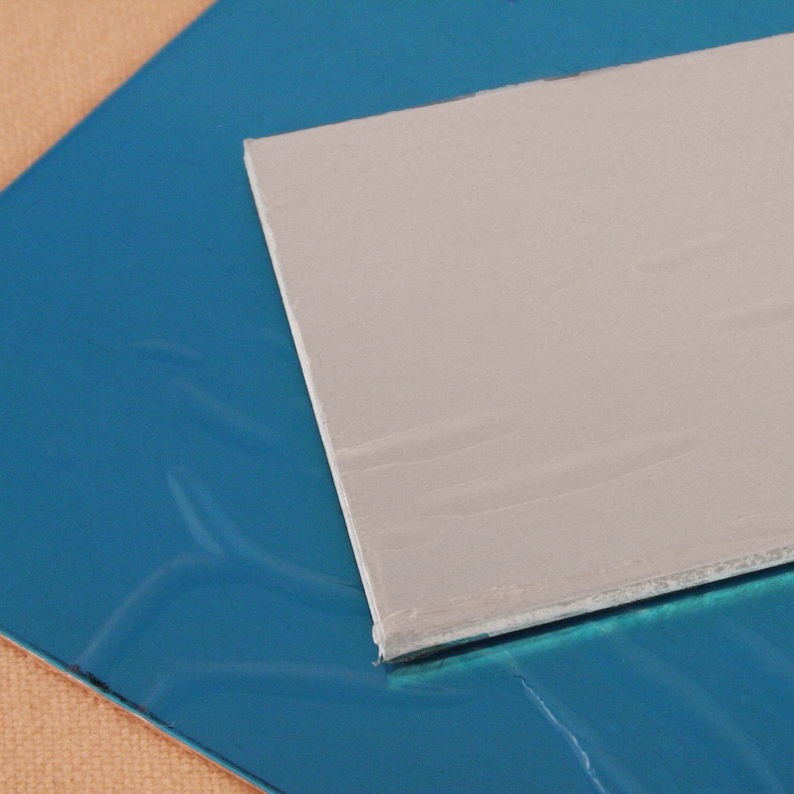 Op de afbeelding: Een close-up van een grijze rechthoekige thermische pasta op een blauw oppervlak.