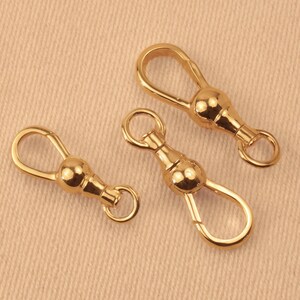 May include: Three gold-toned metal swivel lobster claw clasps, each featuring a smooth, rounded central ball joint, a teardrop-shaped opening mechanism, and a small circular attachment ring at the base for jewelry making or accessory hardware.