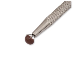 Puede incluir: Una herramienta de plata con una punta de goma marrón y tres puntas. La herramienta se utiliza para recoger objetos pequeños.