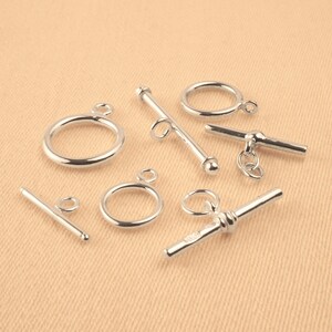 May include: Silver tone metal toggle clasps and rings for jewelry making. The clasps are in various styles, including a T-bar, a bar with a ball end, and a bar with a twisted design.