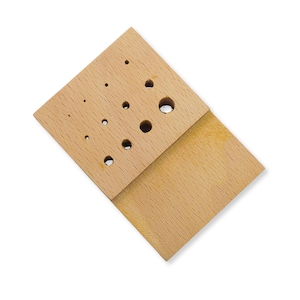 May include: A light-colored wooden block featuring a rectangular base and a raised section with ten circular holes of varying diameters arranged in a grid pattern. The wood grain is visible across the entire surface of the object.