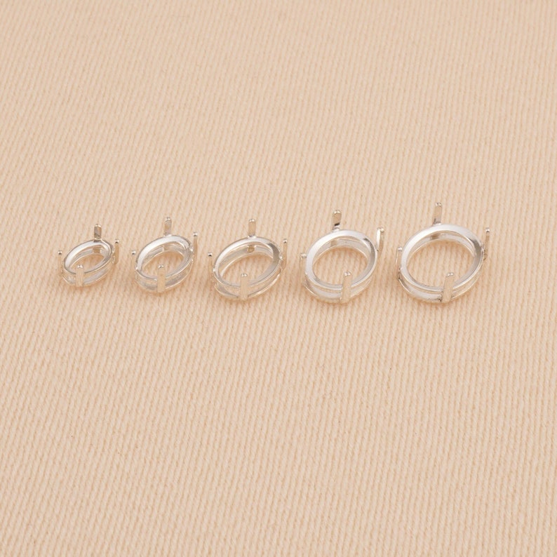 May include: A set of five silver-toned metal oval ring settings arranged in a row from smallest to largest. Each setting features a smooth oval base with four vertical prongs extending upward, designed to hold a gemstone securely in place.