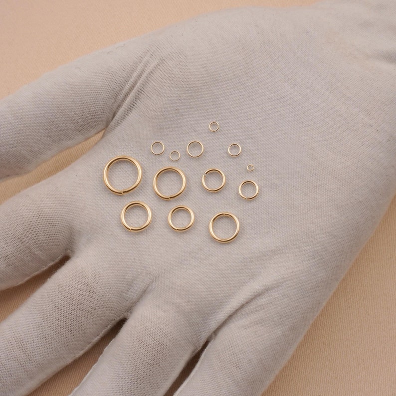 May include: A set of 12 gold jump rings of varying sizes, displayed on a white fabric surface.