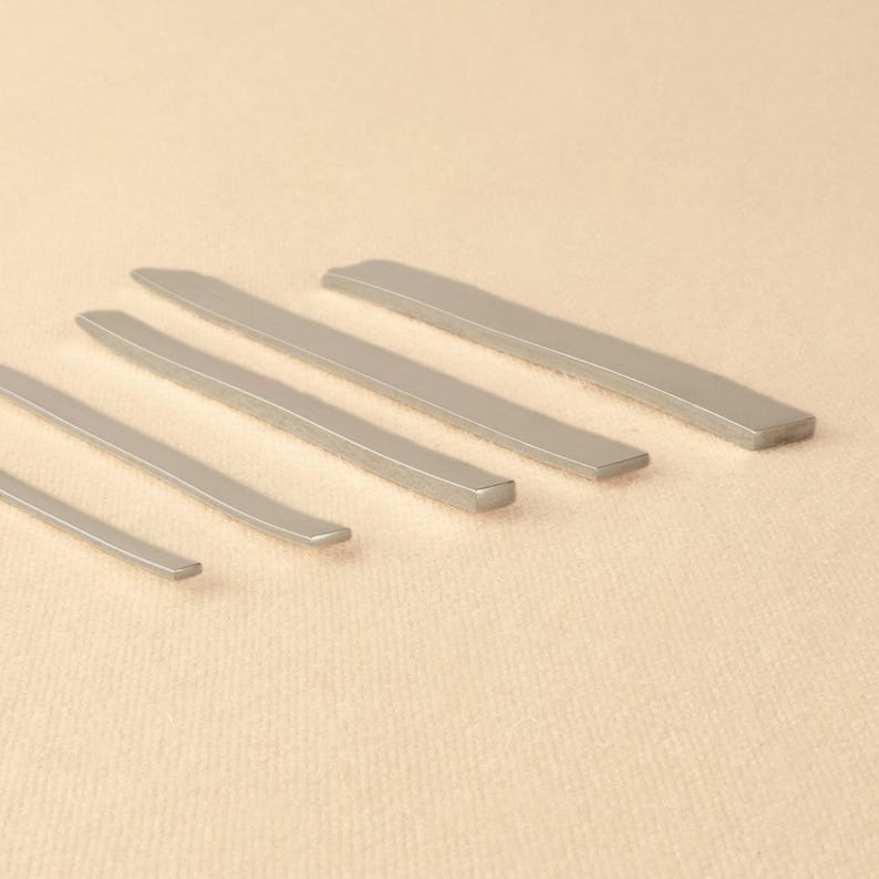 May include: Five silver metal rods of varying lengths, arranged in descending order of size, on a beige surface.