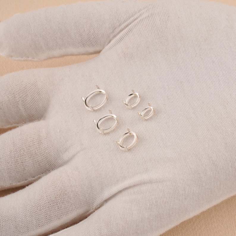May include: Four silver-toned oval jewelry settings with small prongs for securing gemstones. These metal components are arranged in a cluster, featuring varying sizes from larger to smaller, designed for crafting custom jewelry pieces.