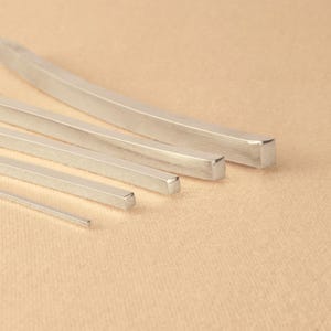 May include: Five silver metal bars of varying widths and lengths, arranged in a graduated size order from largest to smallest. The bars have a smooth, polished finish.