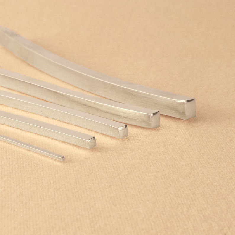 May include: Five silver metal bars of varying widths and lengths, arranged in a graduated size order from largest to smallest. The bars have a smooth, polished finish.