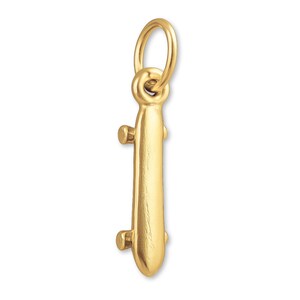 May include: A gold skateboard charm with a loop for attaching to a necklace or bracelet. The charm features a detailed design of a skateboard, including the deck and wheels. This jewellery piece is a fun accessory for skateboard enthusiasts.