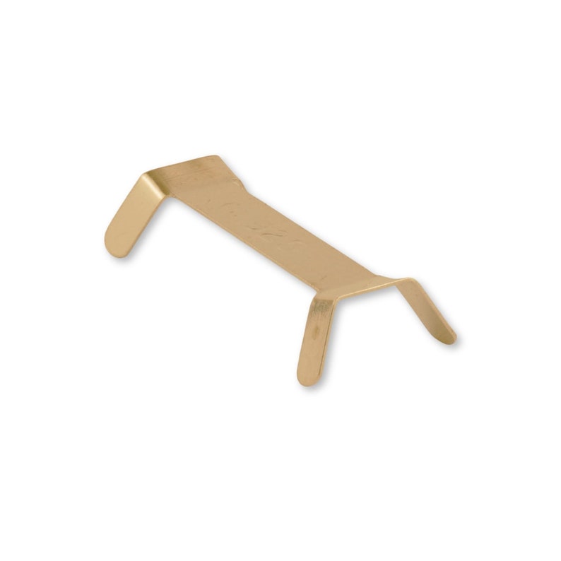 Puede incluir: Un soporte met&aacute;lico de color dorado con un centro rectangular y dos brazos curvos que se extienden hacia abajo. El soporte est&aacute; dise&ntilde;ado para sujetar o sostener un objeto. El art&iacute;culo se muestra sobre un fondo blanco.