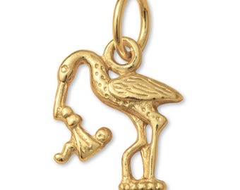 May include: A gold-toned metal charm shaped like a stork carrying a small bundle with a baby inside. The charm features a textured surface on the bird's body and includes a circular jump ring at the top for attachment to a chain or bracelet.