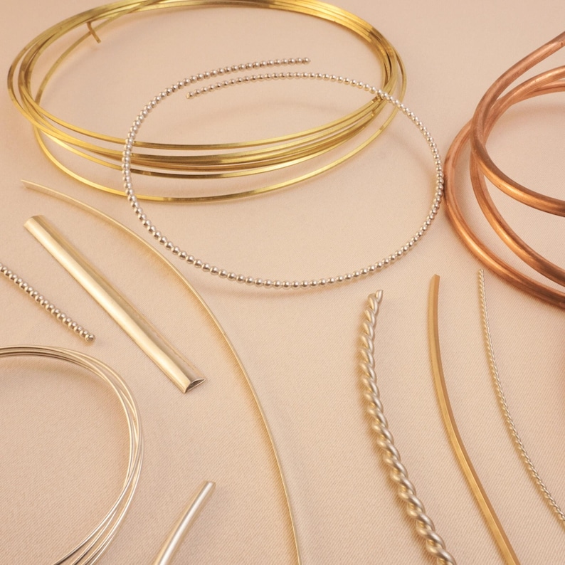 May include: Assortment of gold and copper wire in various shapes and sizes, including round, flat, and twisted wire. The wire is arranged on a light beige surface.