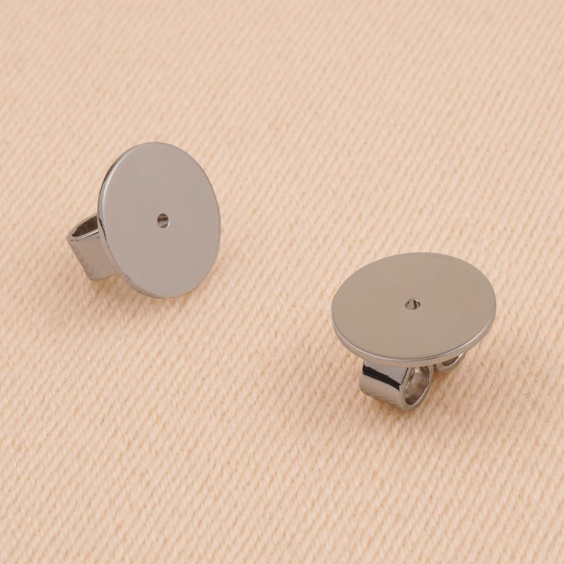 May include: Two silver earring backs with a round, flat surface and a small hole in the center. The backs are designed to be attached to the back of an earring post.
