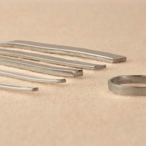 May include: A set of five silver metal rings of varying sizes, with a single larger ring in the foreground.