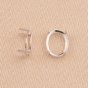 May include: Two silver-colored metal oval-shaped jewelry settings. One setting is shown from a side profile view, revealing its vertical structure, while the other is displayed from a top-down perspective, showing the open oval frame.