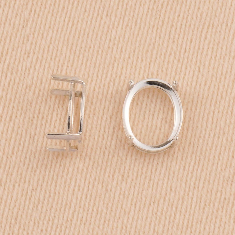 May include: Two silver-colored metal oval-shaped jewelry settings. One setting is shown from a side profile view, revealing its vertical structure, while the other is displayed from a top-down perspective, showing the open oval frame.
