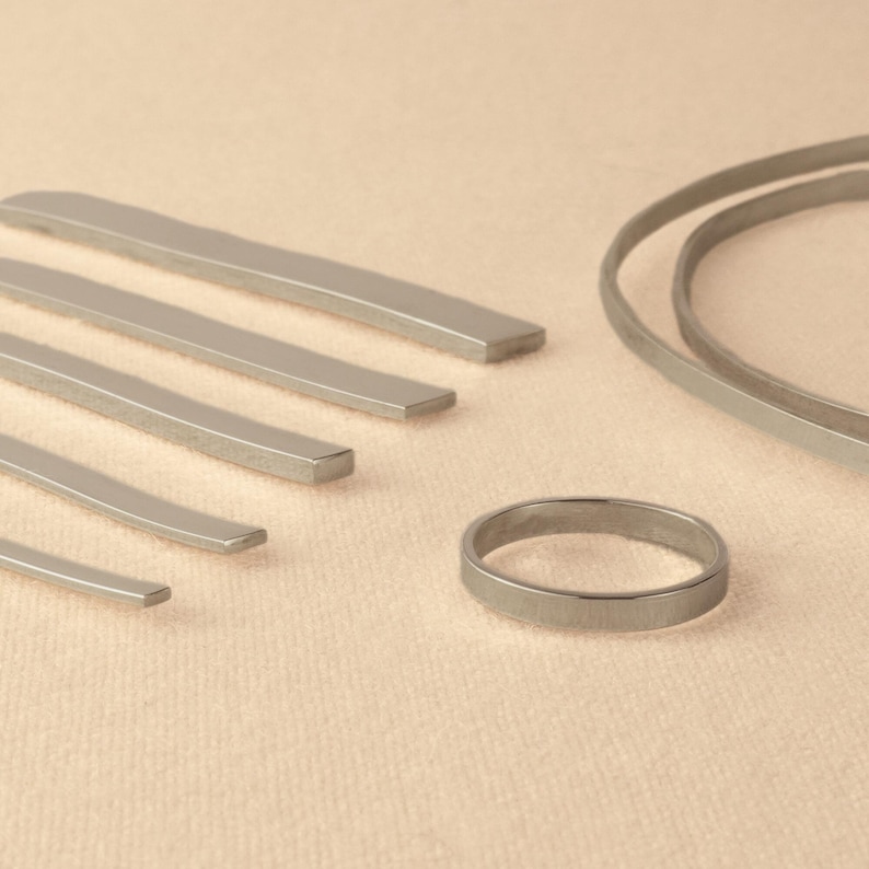 May include: A set of silver metal rings and strips of varying sizes. The rings and strips are arranged on a light beige surface.