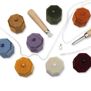 Può includere: Assortimento di otto scatole per anelli in velluto ottagonali in vari colori, tra cui giallo senape, verde, viola, blu, arancione, rosso, beige e una collana a catena d'argento con un ciondolo.