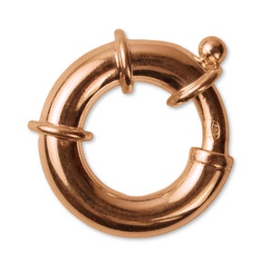 以下が含まれることがあります： 滑らかで丸みを帯びた表面を持つ金色の金属製のリング留め金。留め金は片側に小さな丸いノブがあり、反対側に装飾的なデザインが施されています。