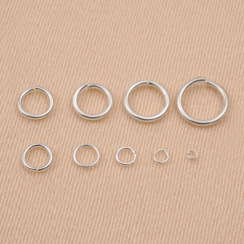 May include: Assortment of silver jump rings in various sizes. The jump rings are arranged in a row from largest to smallest.