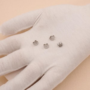 May include: Four silver earring backs on a white surface. The backs are designed to be used with stud earrings.