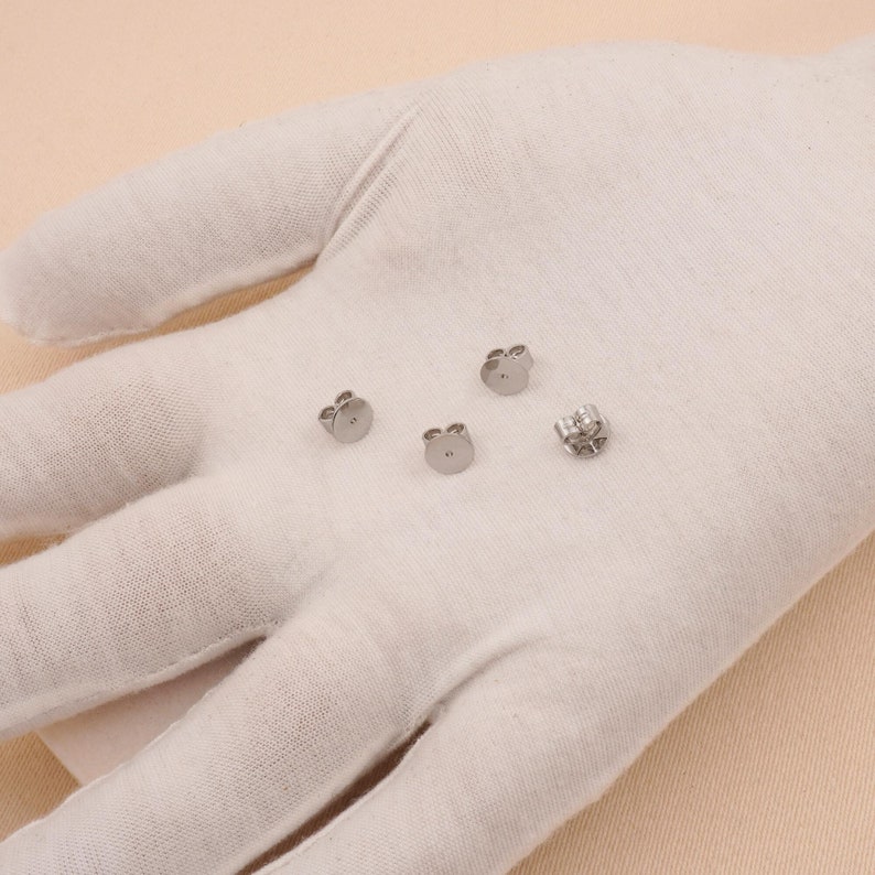 May include: Four silver earring backs on a white surface. The backs are designed to be used with stud earrings.