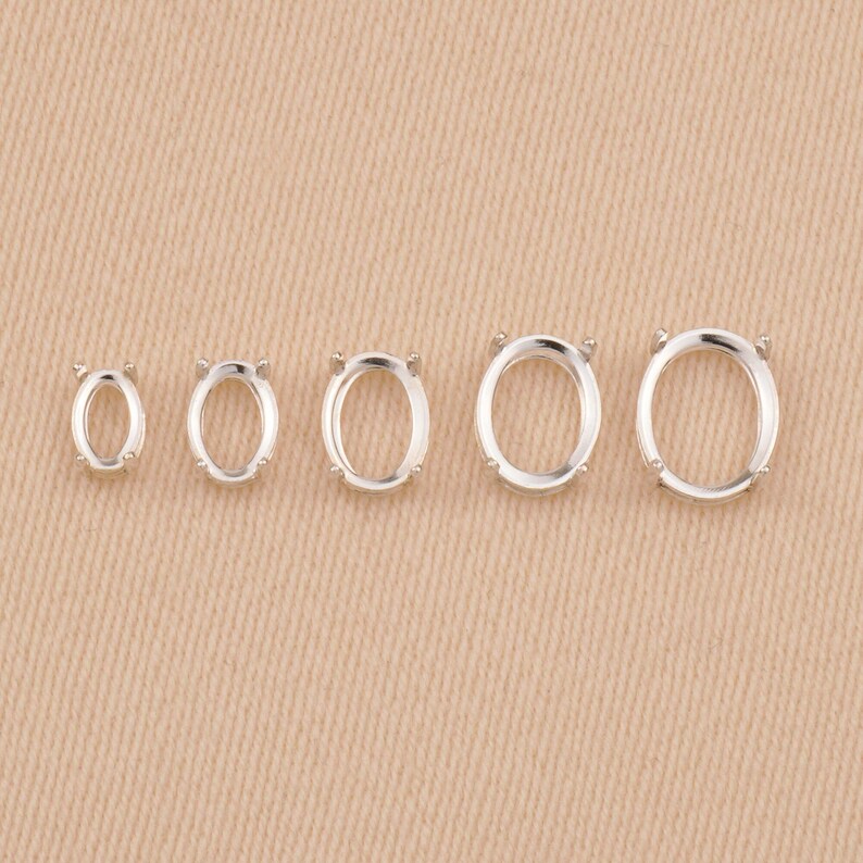May include: Five silver-toned oval-shaped jewelry settings arranged in a horizontal row from smallest to largest. Each setting features four small prongs designed to hold a gemstone securely in place within the open metal frame.