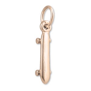May include: A rose gold skateboard charm with a loop for attaching to a necklace or bracelet. The charm has two sets of wheels and is a miniature version of a skateboard. The charm is made of a shiny metal.