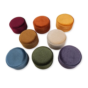 Könnte beinhalten: Acht runde Samt-Ringboxen in verschiedenen Farben, darunter Rot, Orange, Gelb, Beige, Grün, Blau und Lila.