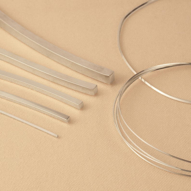 May include: Assortment of silver metal wire and flat bar stock in various sizes and shapes. The wire is coiled and the flat bar stock is straight.