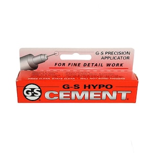 May include: A red tube of G-S Hypo Cement with a white label. The label says "G-S Precision Applicator" and "For Fine Detail Work". It also lists uses for the cement, such as hobbies and crafts, model building, jewelry and beading, fly fishing lures, watch crystals, plastic, glass, metal and ceramic, optical and industrial applications, fine jewelry locking, and general repair. The label also says "Dries Clear, Stays Clear - Will Not Bond Fingers".