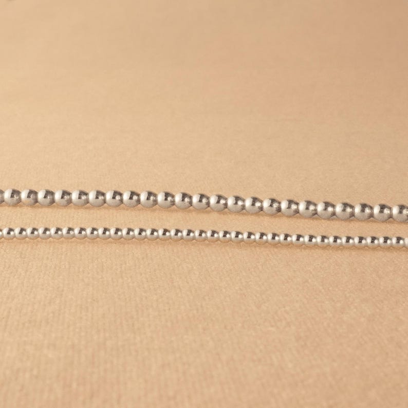 May include: Two silver bead necklaces of different sizes. The larger necklace has larger beads and the smaller necklace has smaller beads.