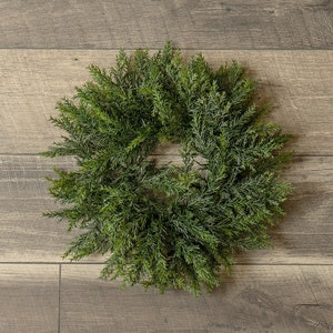 May include: A green artificial evergreen wreath with a natural woodgrain background.