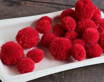 May include: A white ceramic plate filled with red pom-poms. The pom-poms are made of yarn and are soft and fluffy.