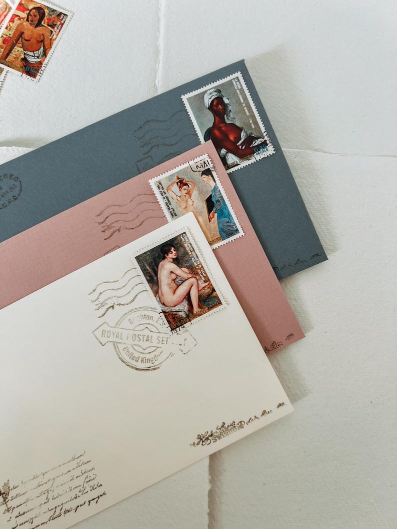 May include: A white envelope with a pink envelope and a blue envelope on top. The white envelope has a stamp with a nude woman on it and a stamp that says "Royal Postal Set - United Kingdom". The pink envelope has a stamp with a woman in a white dress on it and a stamp with a black woman on it. The blue envelope has a stamp with a woman in a white dress on it.