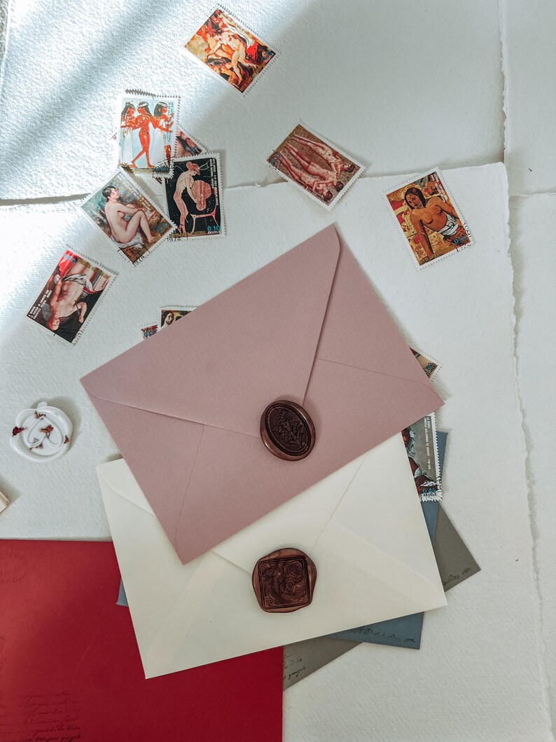 May include: Three envelopes with wax seals. The top envelope is pink, the middle envelope is white, and the bottom envelope is red. The envelopes are on a white surface with vintage postage stamps scattered around them.