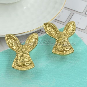 May include: Two gold-toned rabbit-shaped drawer pulls. The rabbit's ears are large and the rabbit's face is detailed with a small nose and eyes.
