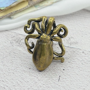 May include: A bronze octopus figurine with detailed tentacles. The octopus is facing forward with its tentacles curled around its body. The figurine is on a white surface.