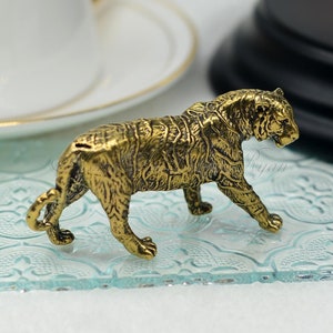 以下が含まれることがあります： 詳細な金色のトラの置物。彫刻には、毛皮の質感や背中のスロットなど、複雑なディテールが施されており、銀行である可能性があります。トラは歩行姿勢でポーズをとっています。