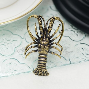 May include: A gold-colored metal lobster figurine. The lobster is detailed with textured claws and a segmented body.