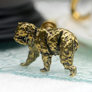 May include: A gold-colored bear figurine with a detailed textured surface. The bear is standing on a glass surface with a decorative pattern.