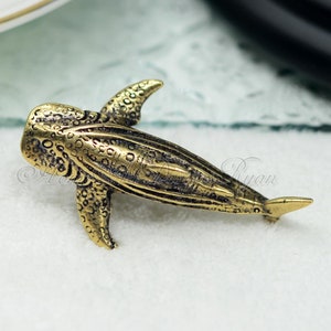 Op de afbeelding: Een gouden metalen walvishaai-beeldje. Het beeldje is gedetailleerd met een getextureerd oppervlak en een licht geopende mond.