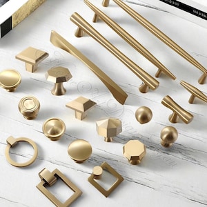 Puede incluir: Una colecci&oacute;n de herrajes dorados para gabinetes, que incluyen perillas y tiradores, en varias formas y tama&ntilde;os. Los herrajes incluyen dise&ntilde;os redondos, cuadrados y geom&eacute;tricos. Los tiradores son largos y delgados, mientras que las perillas son m&aacute;s compactas.