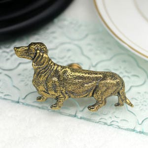 Peut inclure: Une figurine de dachshund dorée, une représentation détaillée et réaliste d'un chien, avec une surface texturée.
