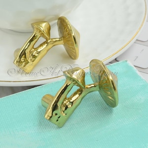 May include: Two gold mushroom-shaped cabinet knobs. The knobs are made of metal and have a detailed design.