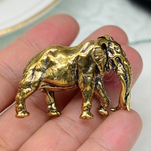 May include: A gold-colored elephant figurine with detailed features. The elephant is standing on all four legs with its trunk raised.